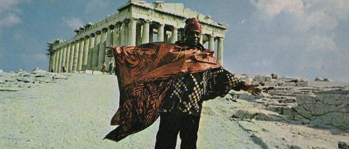 A man in african garb standing in front of the Parthenon