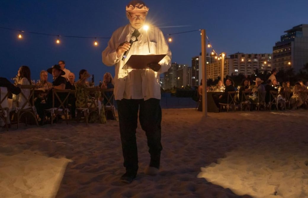 A man speaking in front of a group on the beach at night